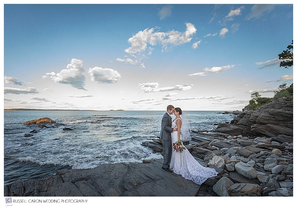 bride and groom kissing on the rocks at the ocean