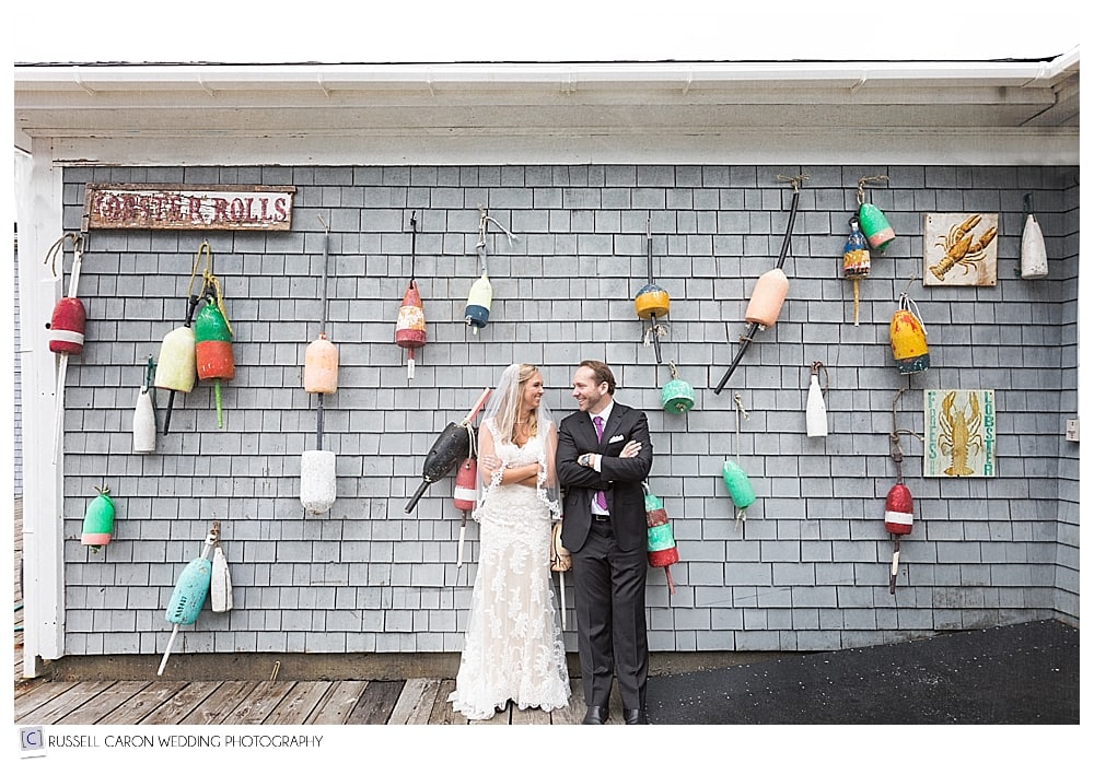 bride and groom leaning against wall with lobster bouys