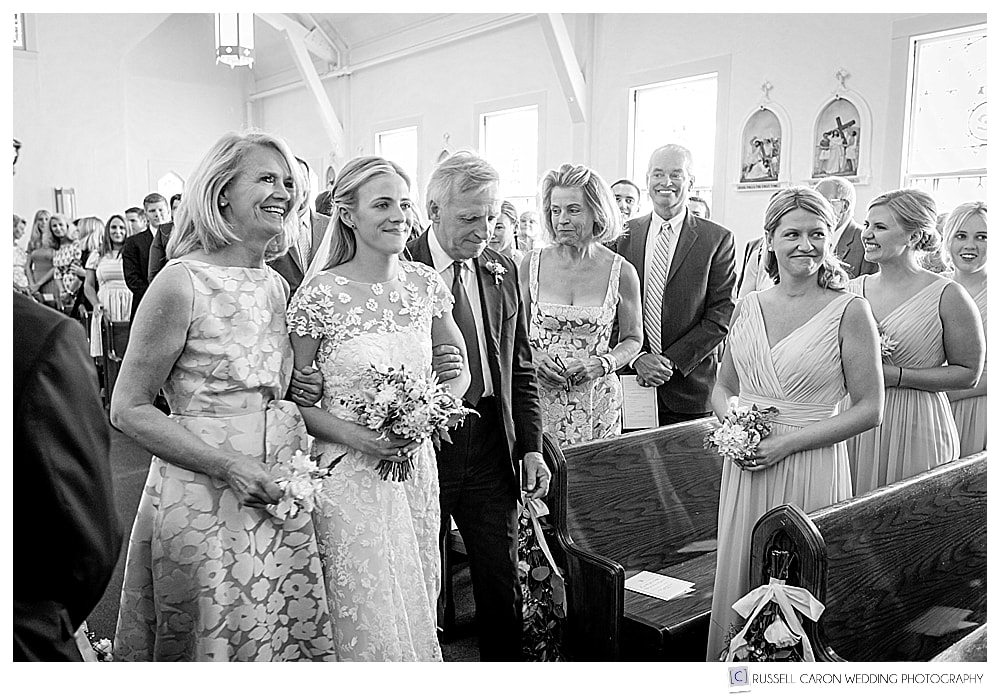 black and white photo of bride and her parents walking down the aisle at Our Lady of Good Hope Church, in Camden, Maine
