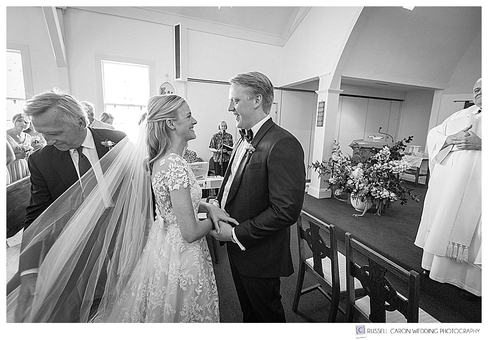 black and white photo of a groom greets the bride as she arrives at the altar at Our Lady of Good Hope Church, Camden, Maine