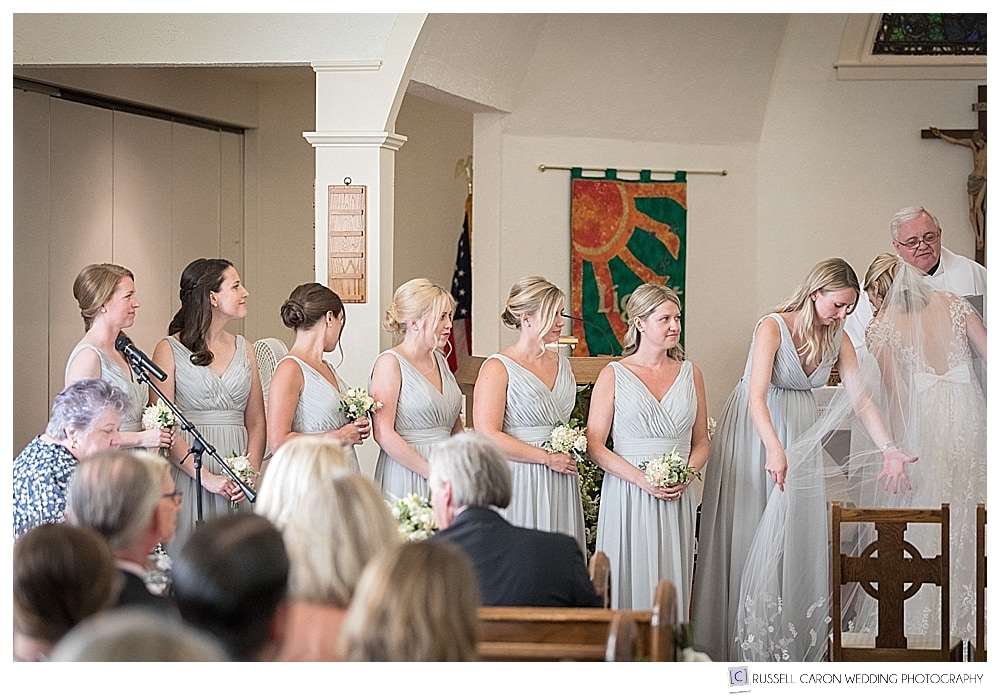 bridesmaids stand at the altar during a wedding ceremony at Our Lady of Good Hope Church, Camden, Maine