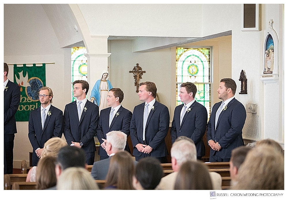 groomsmen stand at the altar during a wedding ceremony at Our Lady of Good Hope in Camden, Maine