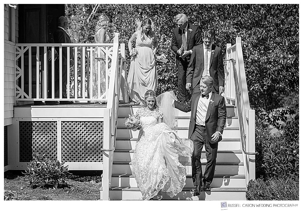 black and white photo of bride and groom walking down the stairs, with bridal party behind them