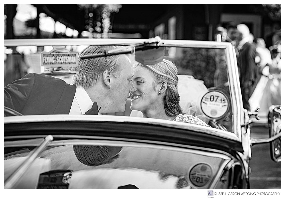 black and white photo of bride and groom kissing in antique convertible