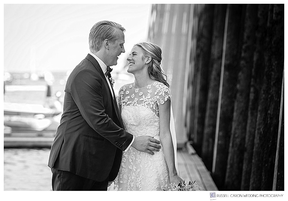 black and white photo of bride and groom smiling at each other, standing on a dock in Camden, Maine
