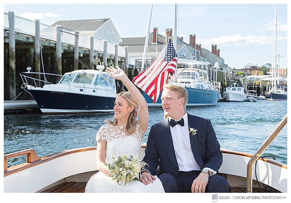 bride and groom sitting in the back of a boat, waving 