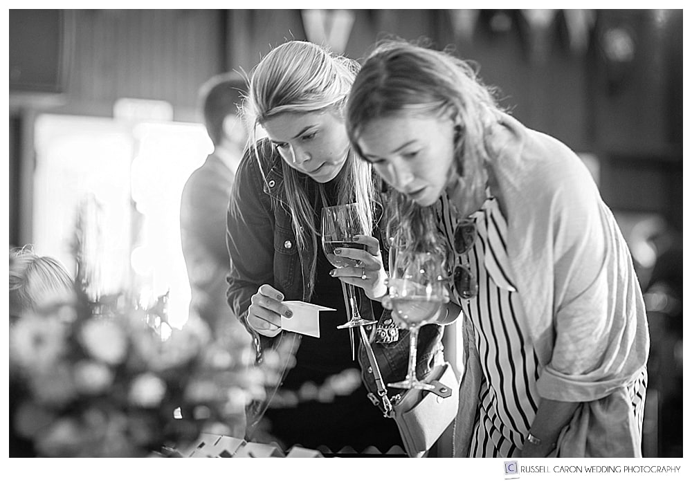 black and white photo of women sipping wine, looking at something on a table