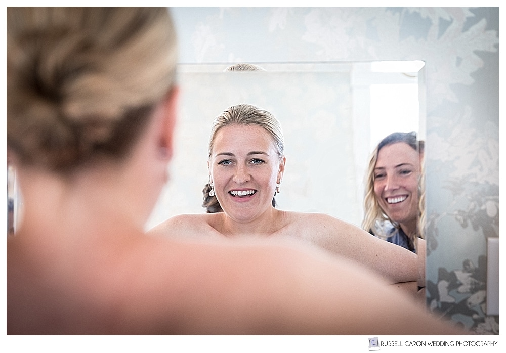 bride looking at her self in a mirror, while she puts on her wedding dress