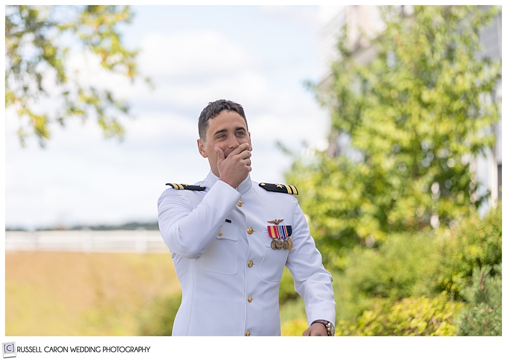 groom in dress whites, walks toward his bride, his hand to his mouth