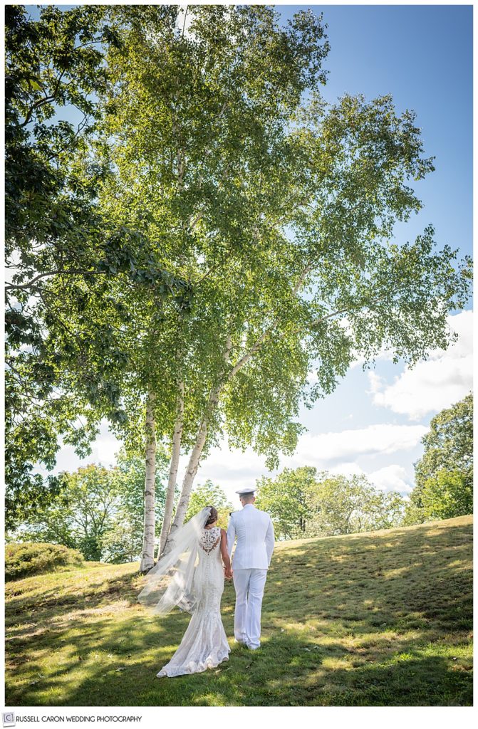 bride and groom walking away from the camera, up a hill lined with trees