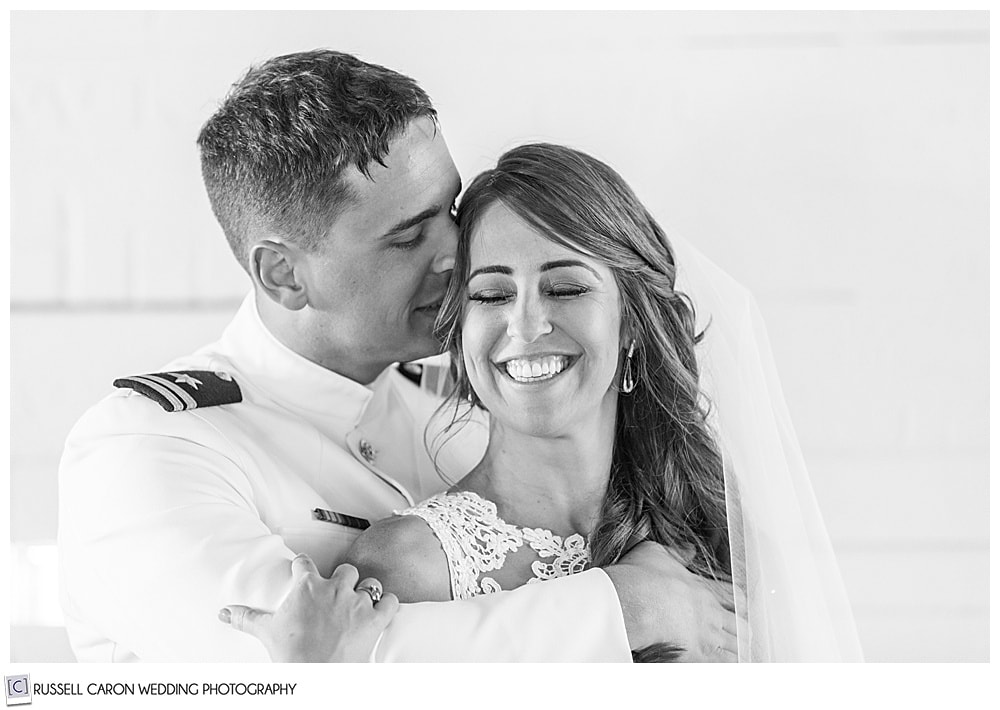 black and white photo of groom whispering in bride's ear, as she smiles