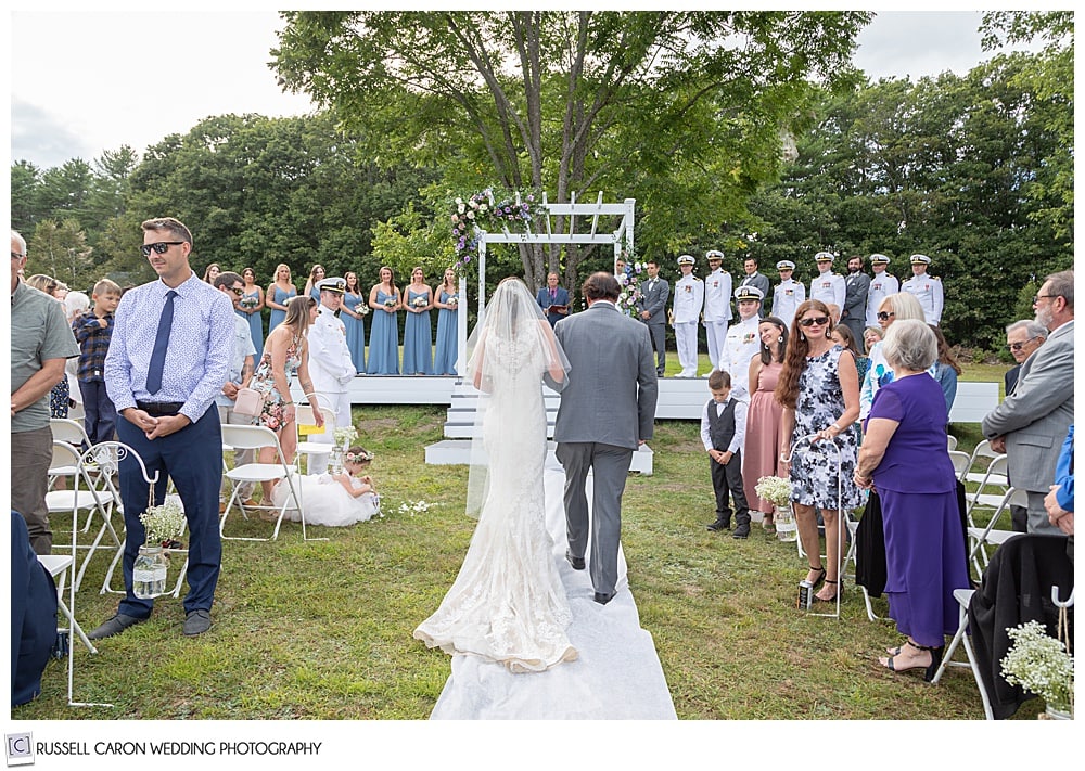 bride and her father, backs to the camera, walk toward the groom at their backyard ceremony site