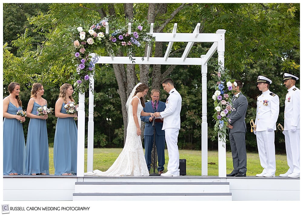 groom puts ring on the bride's finger during their backyard Dresden Maine wedding ceremony