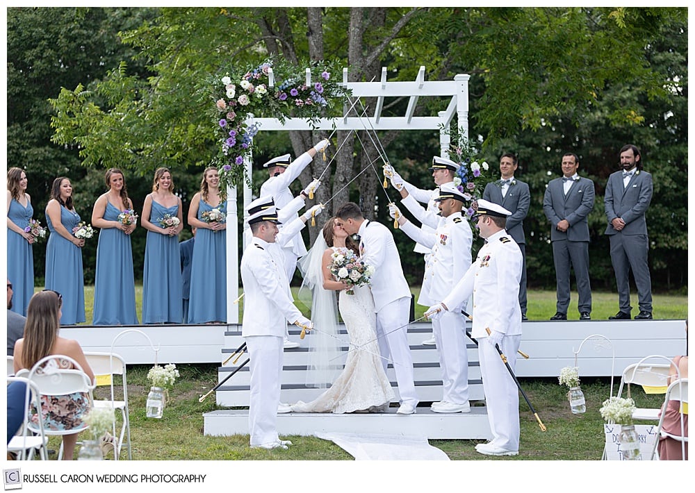 bride and groom kiss under the sword arch of groomsmen in their dress whites