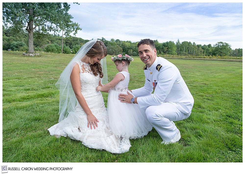 flower girl playing with bride's dress, as she sits on the ground with the groom