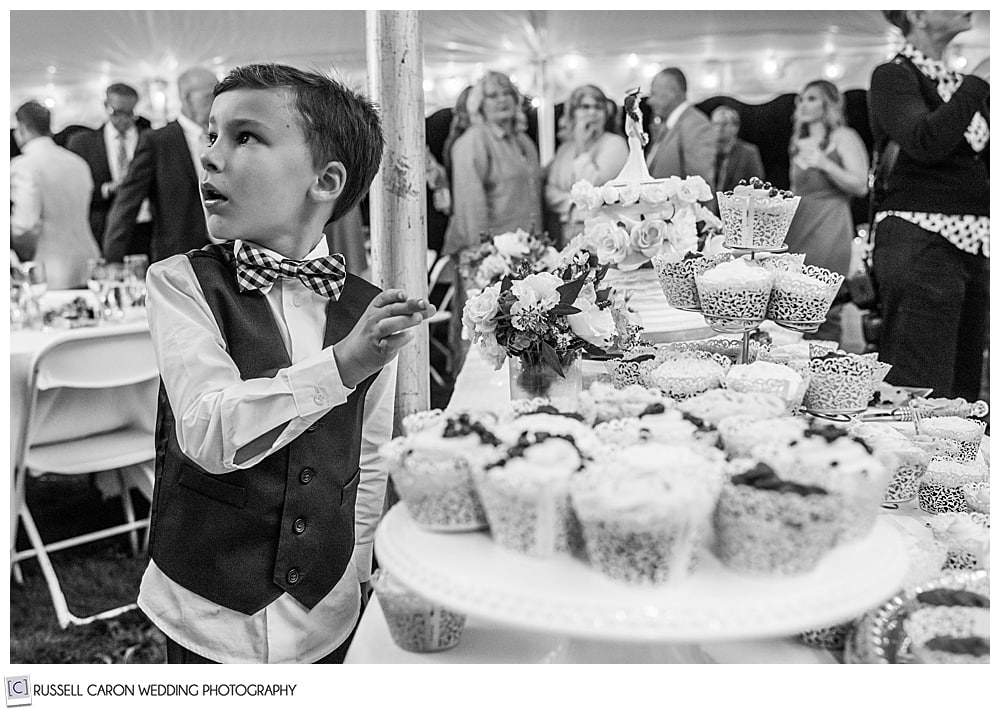 black and white photo of a boy reaching for a cupcake at a wedding, with turned head and surprised look