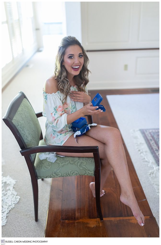 bride sitting in a chair, opening a gift with her hand to her heart