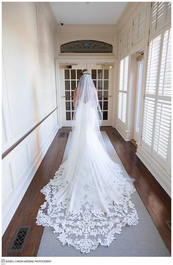 bride in a long white dress with lace edges, and long white veil in a hallway