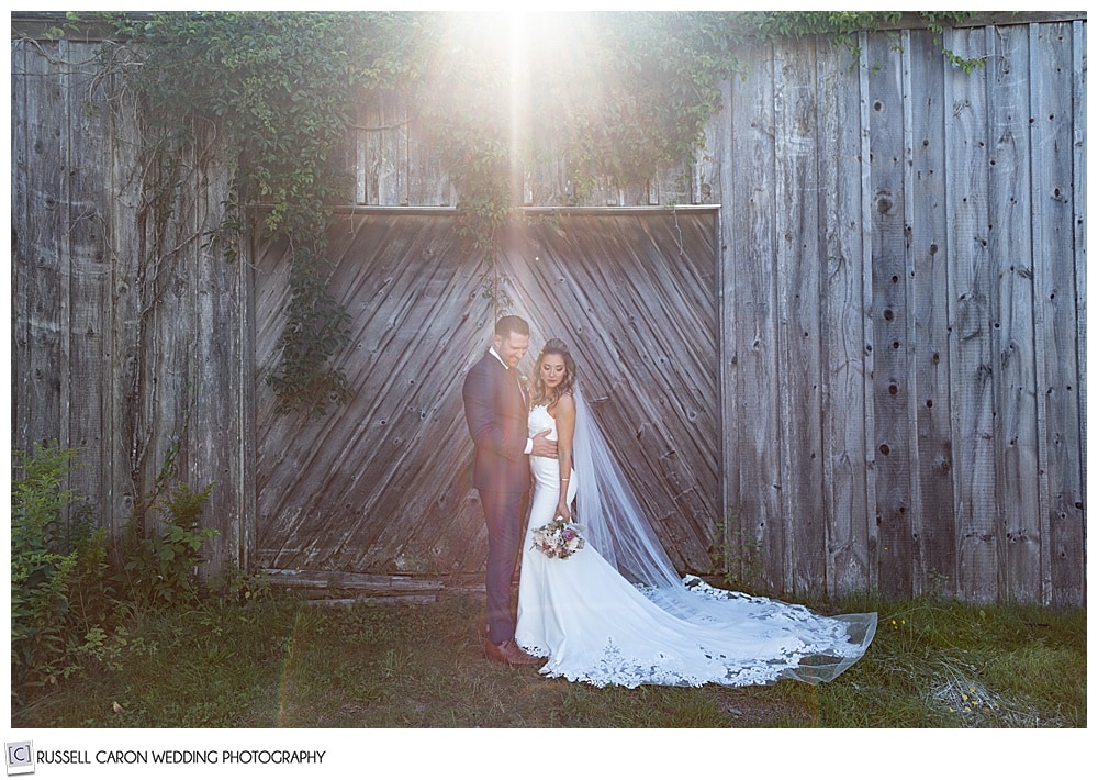 bride and groom in front of an old barn, bride is looking down, groom is looking at the bride