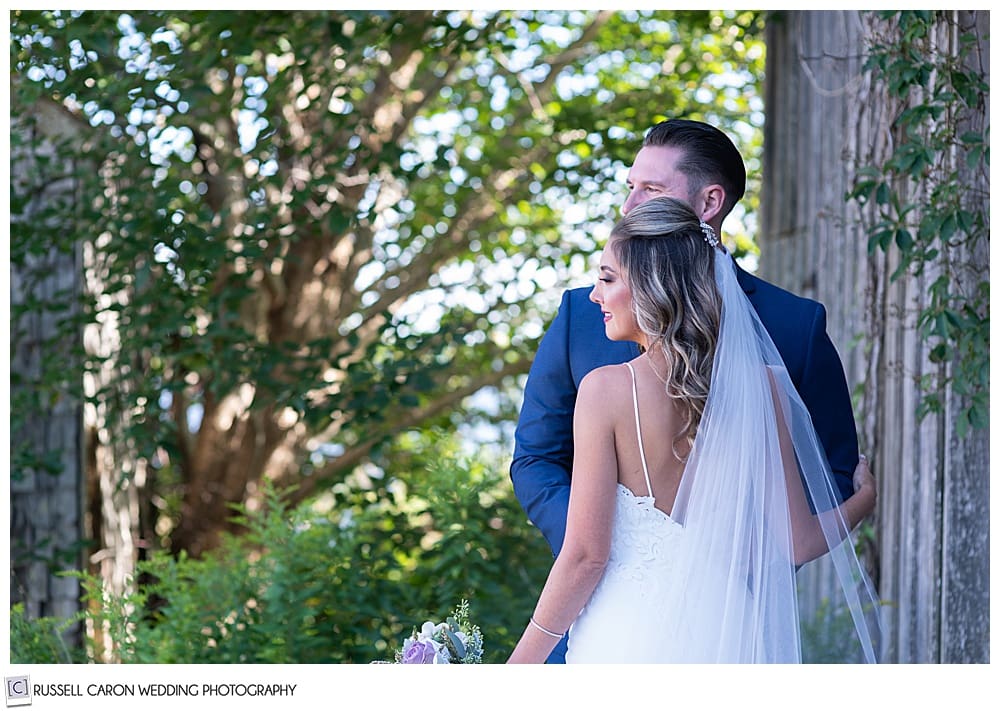 back view of a bride standing next to her groom, with a beautiful tree in the background