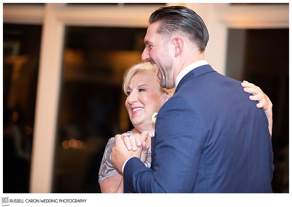 groom dancing with his mother, they're side to the camera, she is smiling, he has his mouth in an open smile