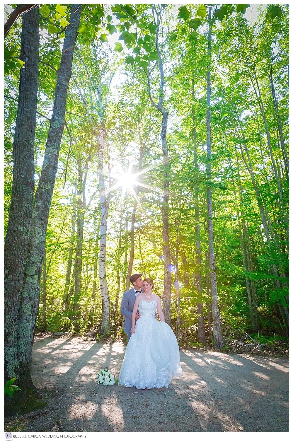 bride and groom standing amid the trees, with the sun behind them