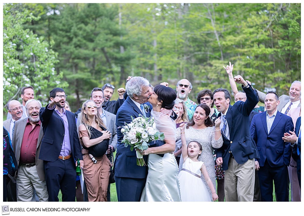 bride and groom kissing while surrounded by friends and family