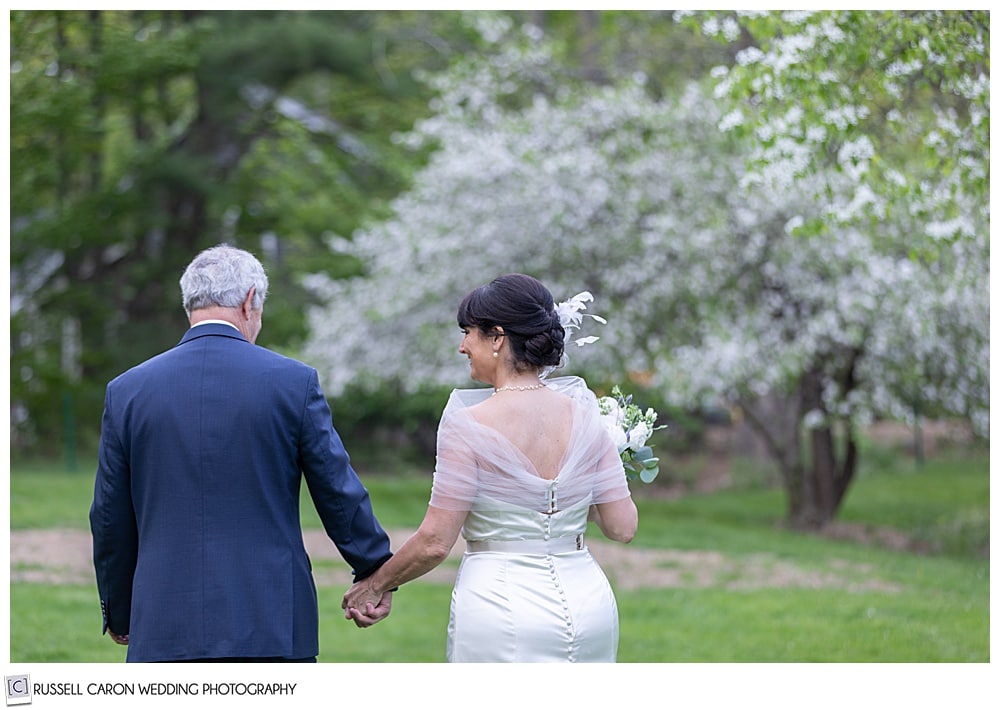 bride and groom holding hands and walking away in an apple orchard