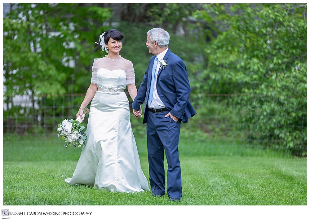 bride and groom holding hands and walking in a grassy field