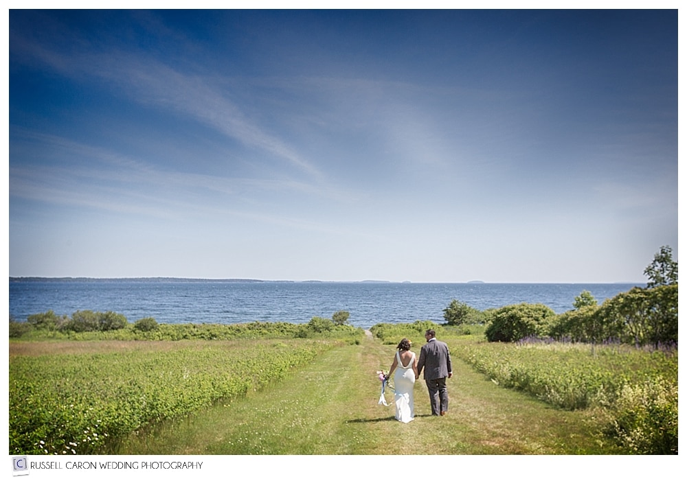 bride-and-groom-walking-hand-in-hand-in-field
