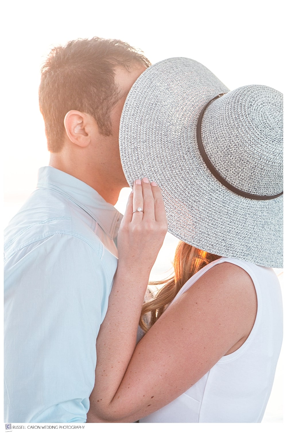 man and woman kissing behind a hat