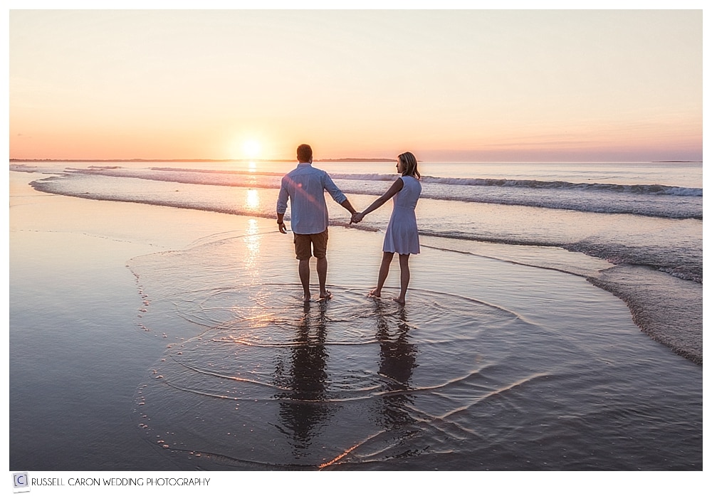 man and woman holding hand and walking in the ocean at sunrise