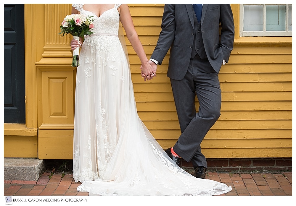 bride and groom standing in front of yellow colonial house