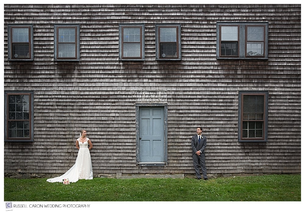 bride and groom standing apart in front of colonial house