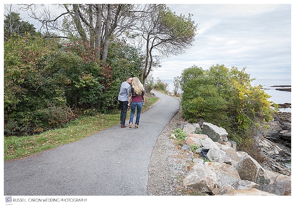 couple walking on Marginal Way during Perkins Cove engagement session in Ogunquit Maine