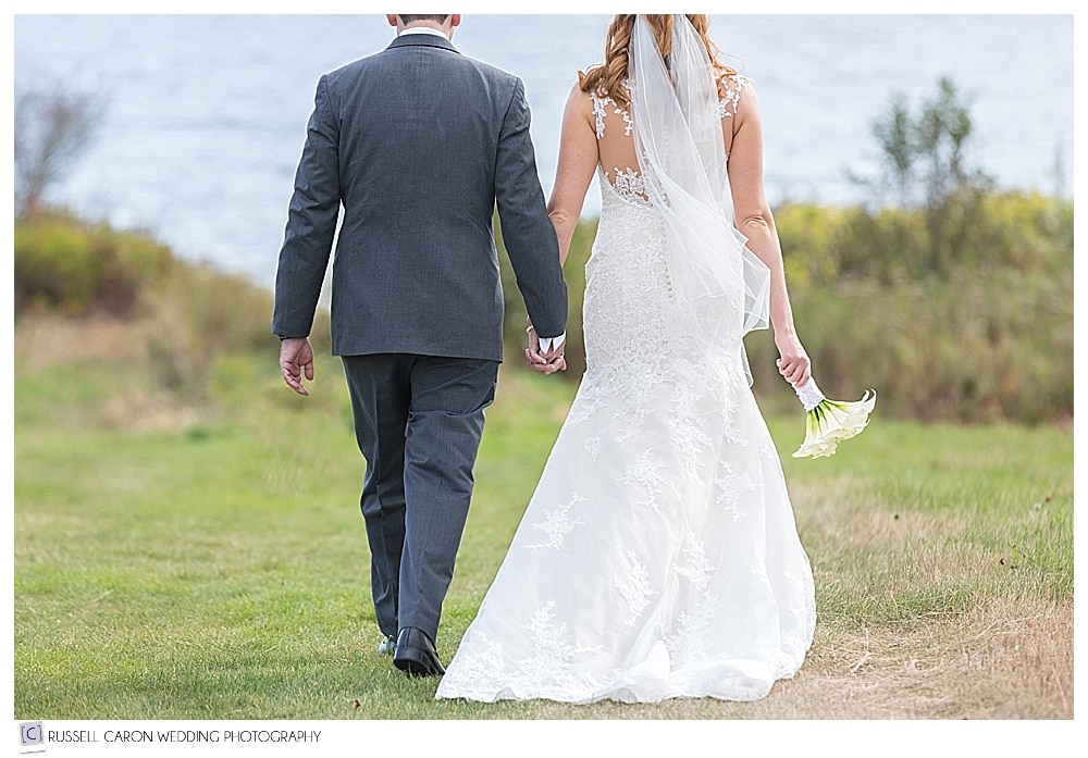 bride and groom walking in a field towards the ocean