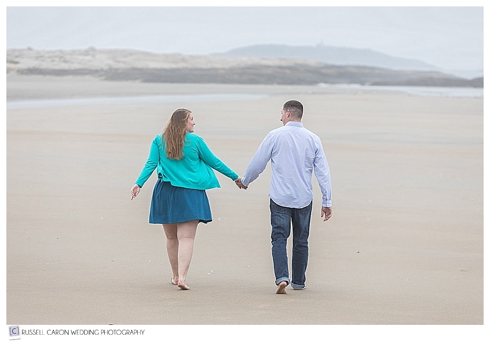 man and woman walking hand in hand during their Popham Beach engagement session