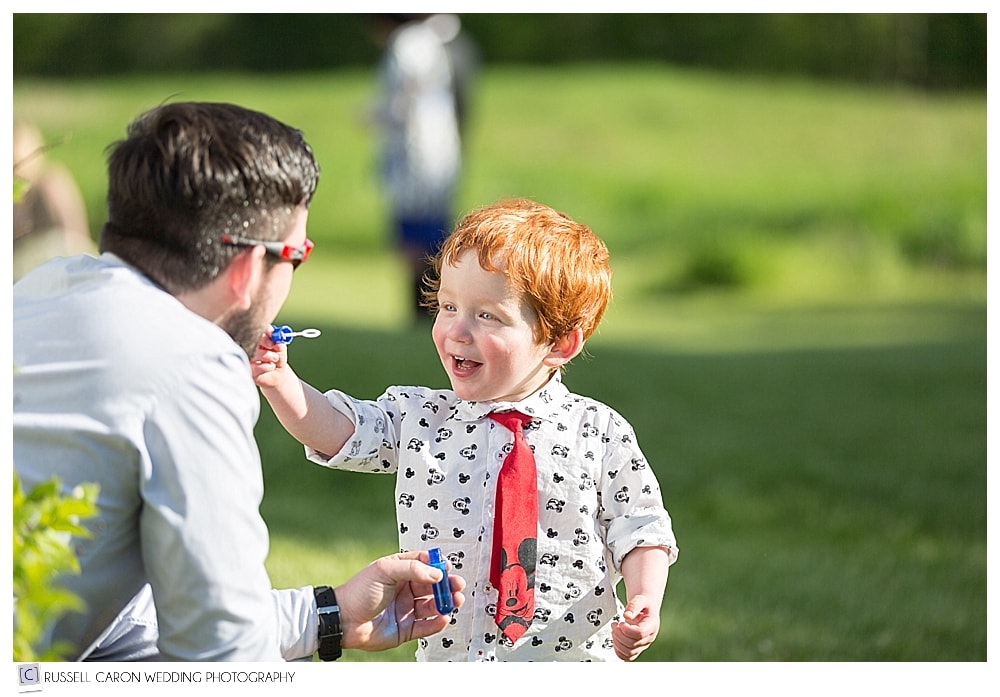 Little boy with dad blowing bubbles at outdoor wedding reception