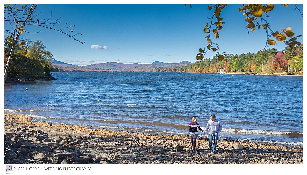 couple holding hands and walking near lake with fall foliage