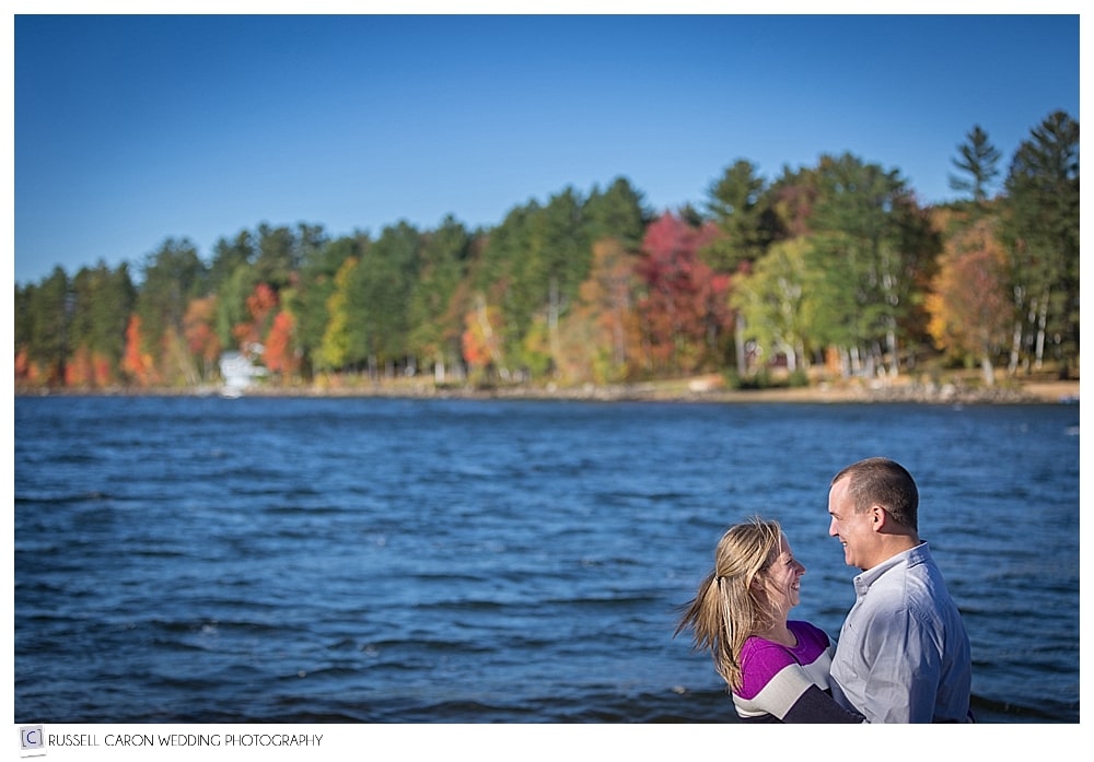 couple facing each other near lake with fall foliage