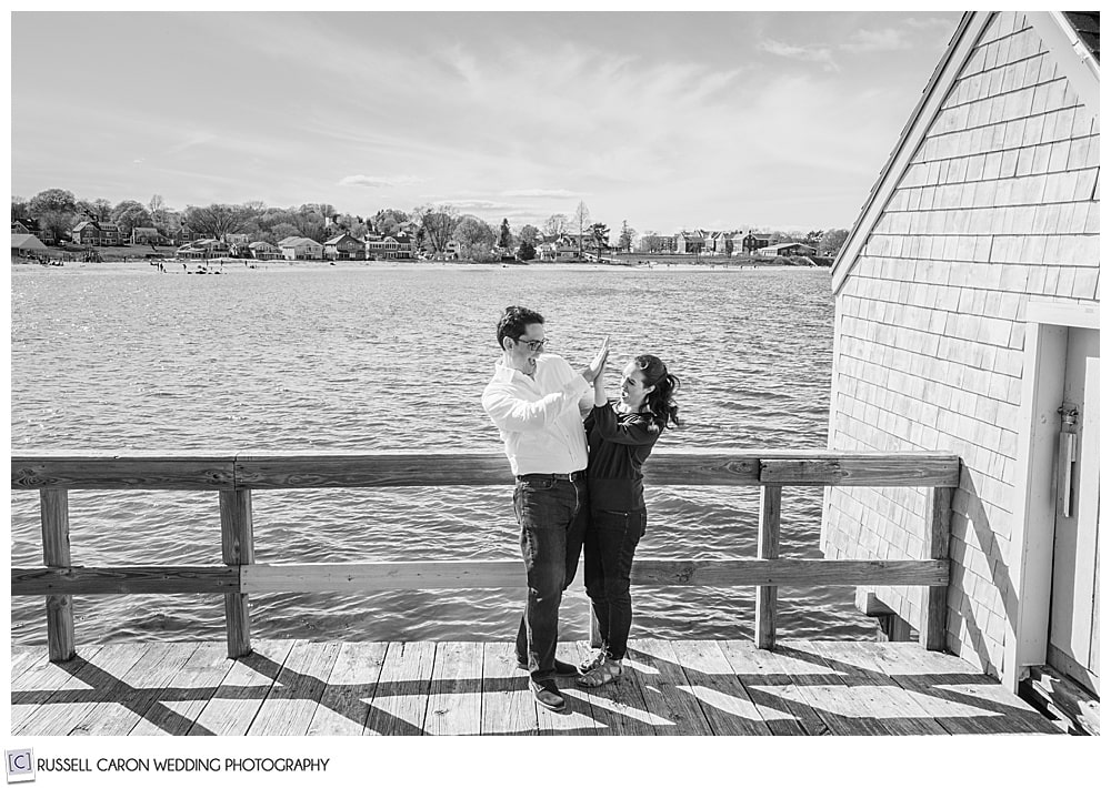 a black and white photo of a man and woman giving each other a high five at willard beach engagement session