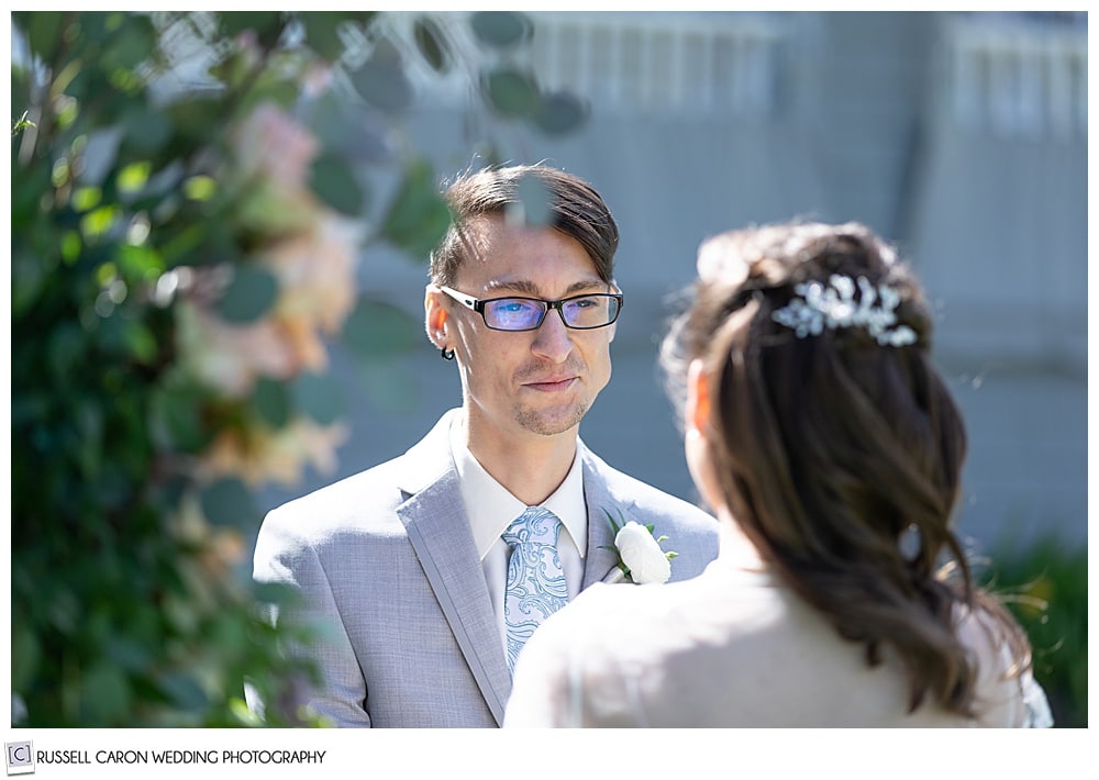 groom, wearing glasses and a gray tux, looking at his bride