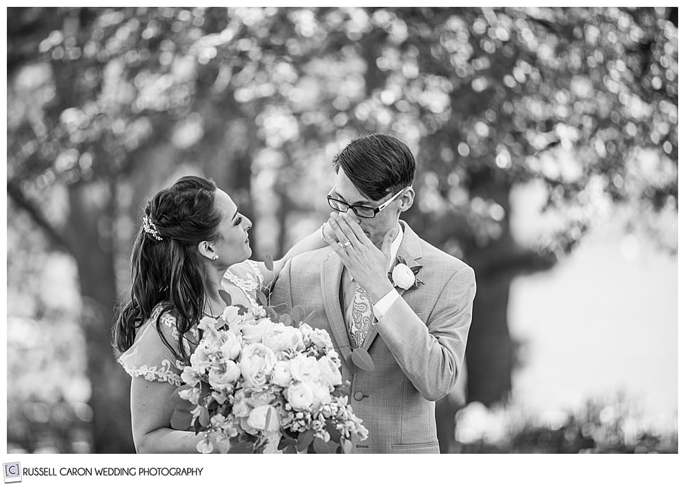 black and white photo of groom wiping his eyes as his bride looks on