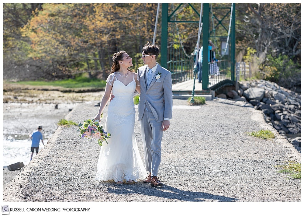 bride and groom walking near the Wiggley Bridge,  with their arms around each other