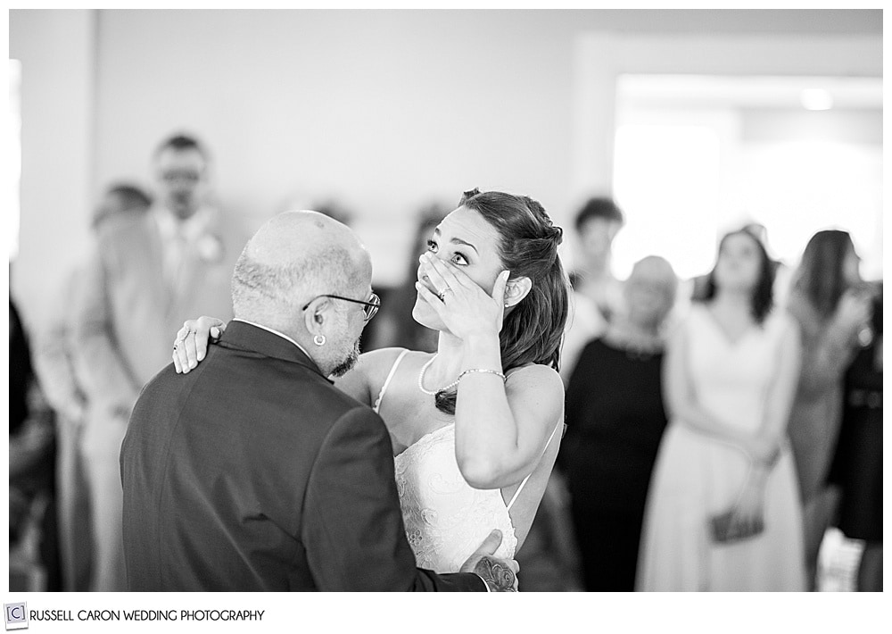 black and white photo of bride wiping her eye as she dances with her stepfather