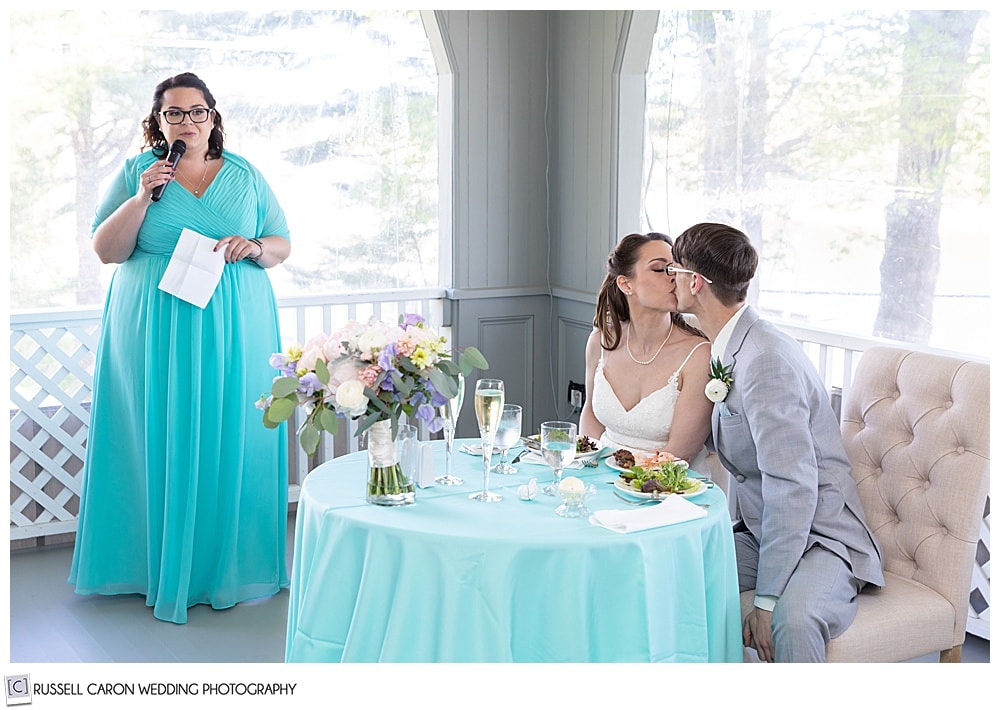 bride and groom kissing as maid of honor looks on