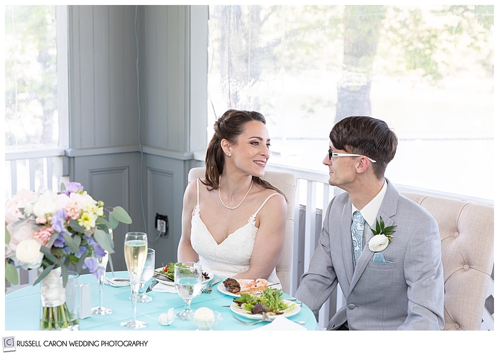 bride and groom looking at each other, while they sit at their sweetheart table