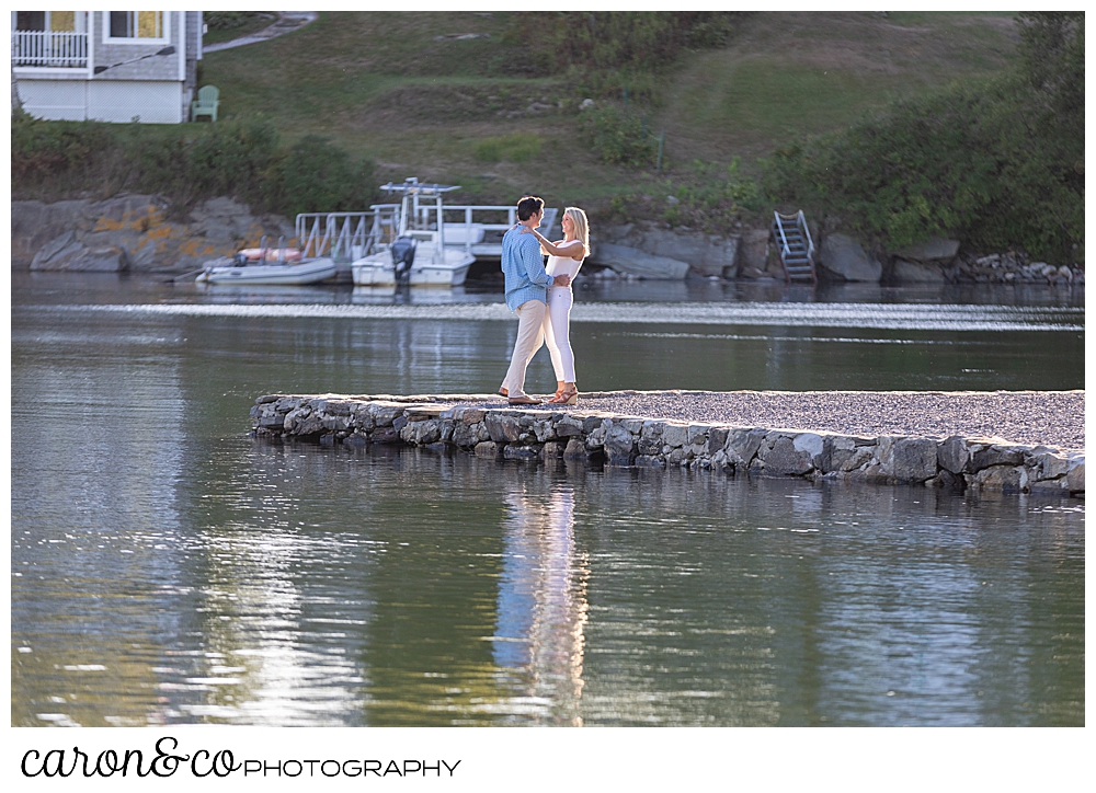 a man and woman are standing face to face, at the water's edge during a Boothbay Harbor engagement session