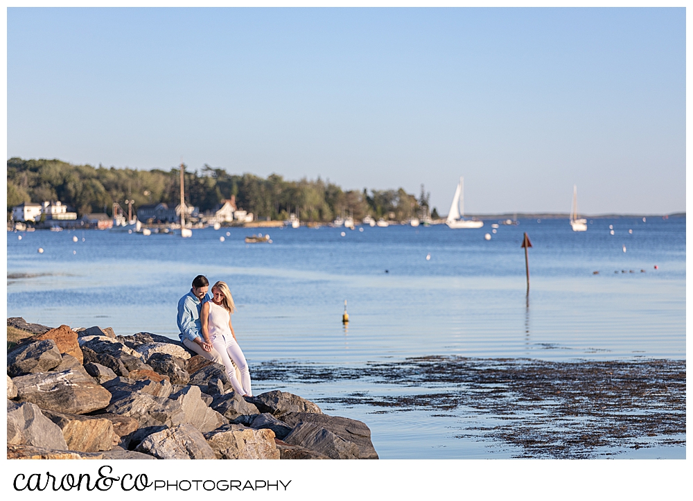 A man and woman are sitting on the rock in Boothbay Harbor, Maine during a Boothbay Harbor engagement