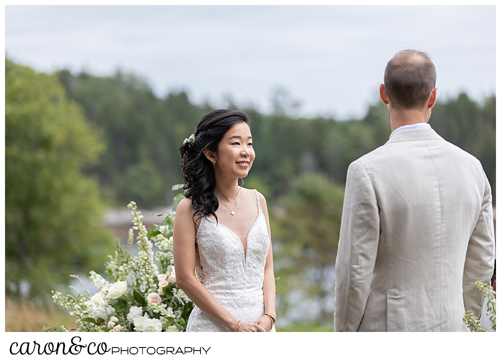 bride smiles at the groom during a Grey Havens Inn wedding ceremony, on the lawn at Georgetown Maine